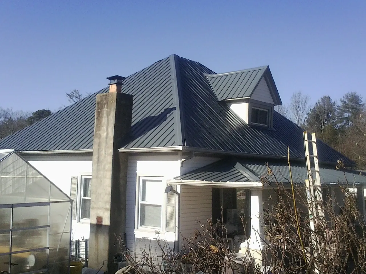 Dark blue standing seam metal roof on a white farmhouse with dormer — Slate & Tile Roof Repair by Roofing Brothers in Tuttle