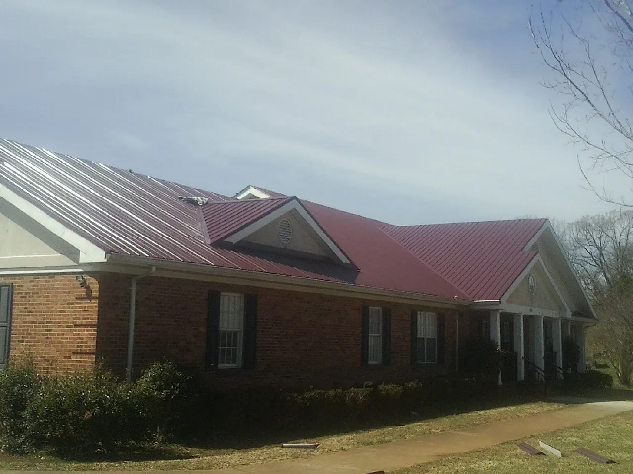 Red metal roof with gabled entries on a long brick building, from a Hail Damage Roof Repair job in Tuttle