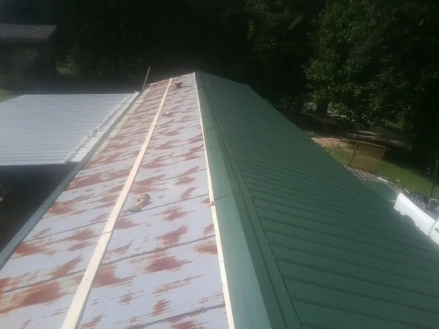 Old rusted panels beside newly installed green metal roofing — Wind Damage Roof Repair by Roofing Brothers in Tuttle