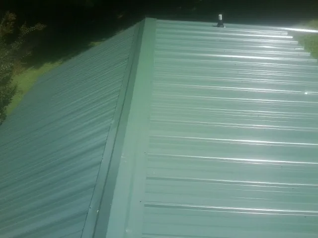 New green metal panels meeting at the ridge of a roof — Flat Roof Repair work by our crew in Tuttle
